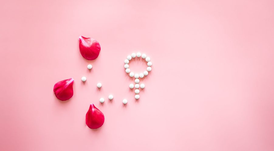 Gender Venus symbol made of pills, and peony flower petals on a pink background, woman period and health concept.